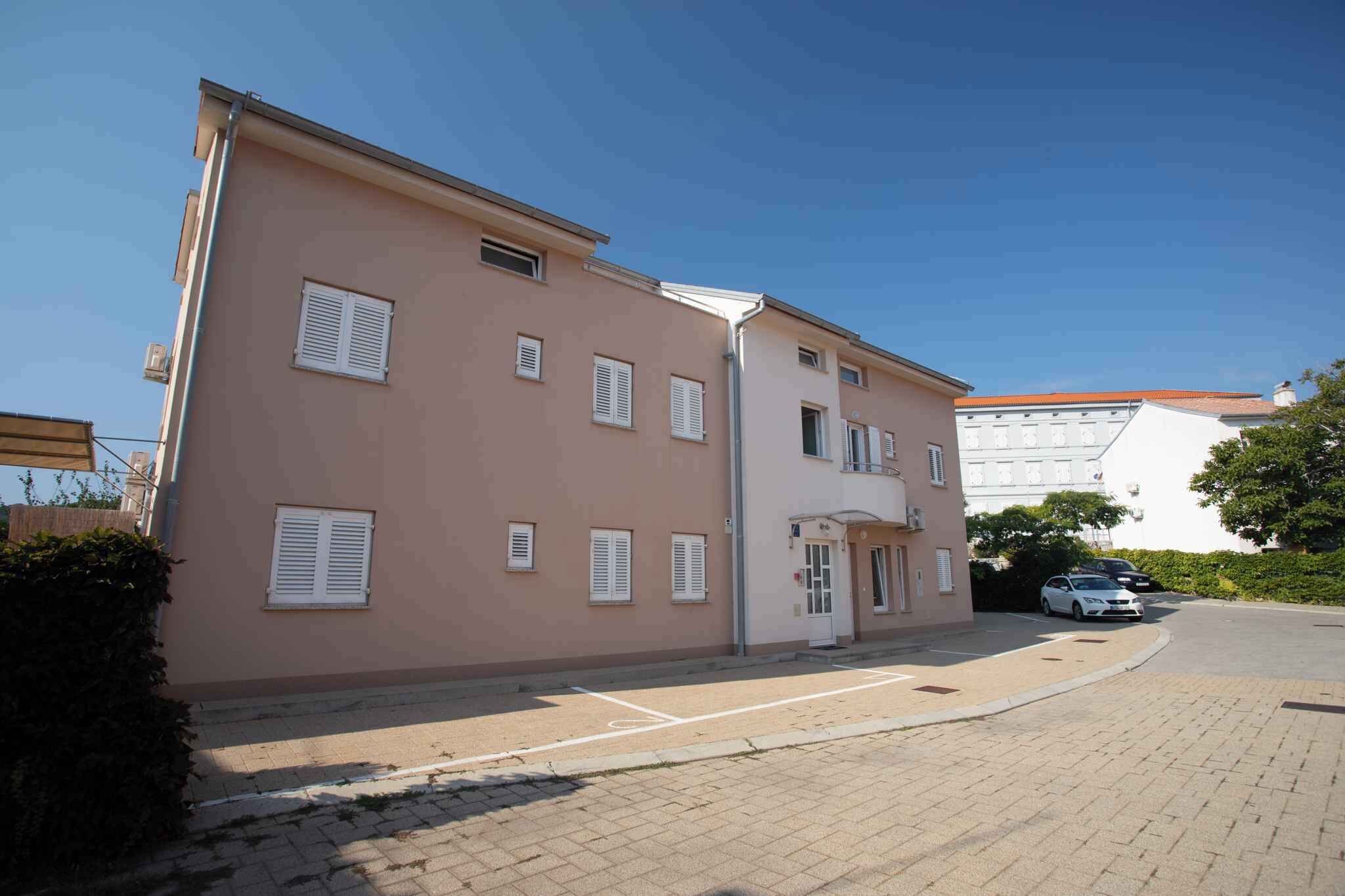 En toetages bygning med flad facade, flere vinduer med lukker og en parkeringsplads foran.