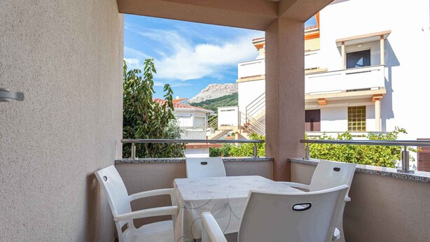 Un balcon avec une table et des chaises, offrant une vue sur un paysage montagneux et les bâtiments environnants.