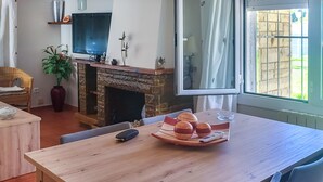 Ein gemütliches Wohnzimmer mit Kamin, Fernseher und Esstisch mit Brot und Fernbedienung.