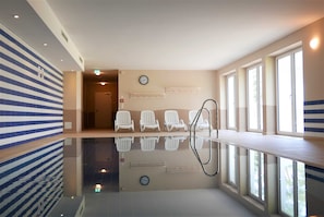 Ein moderner Poolbereich im Innenbereich mit spiegelndem Boden, Sitzgelegenheiten am Pool und großen Fenstern für natürliches Licht.