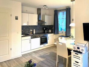 Eine moderne Küche mit weißen Schränken, einem eingebauten Backofen und einem Essbereich mit weißem Tisch und Stuhl.