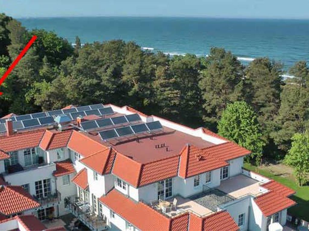 Un immeuble résidentiel doté de plusieurs toits recouverts de tuiles rouges, de panneaux solaires et offrant une vue sur la mer.