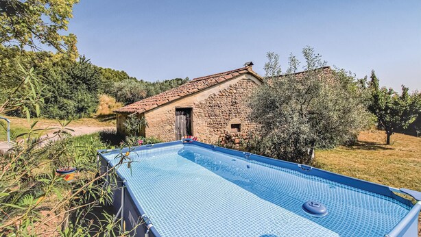 A stone building with a tiled roof, a swimming pool, and surrounding greenery.