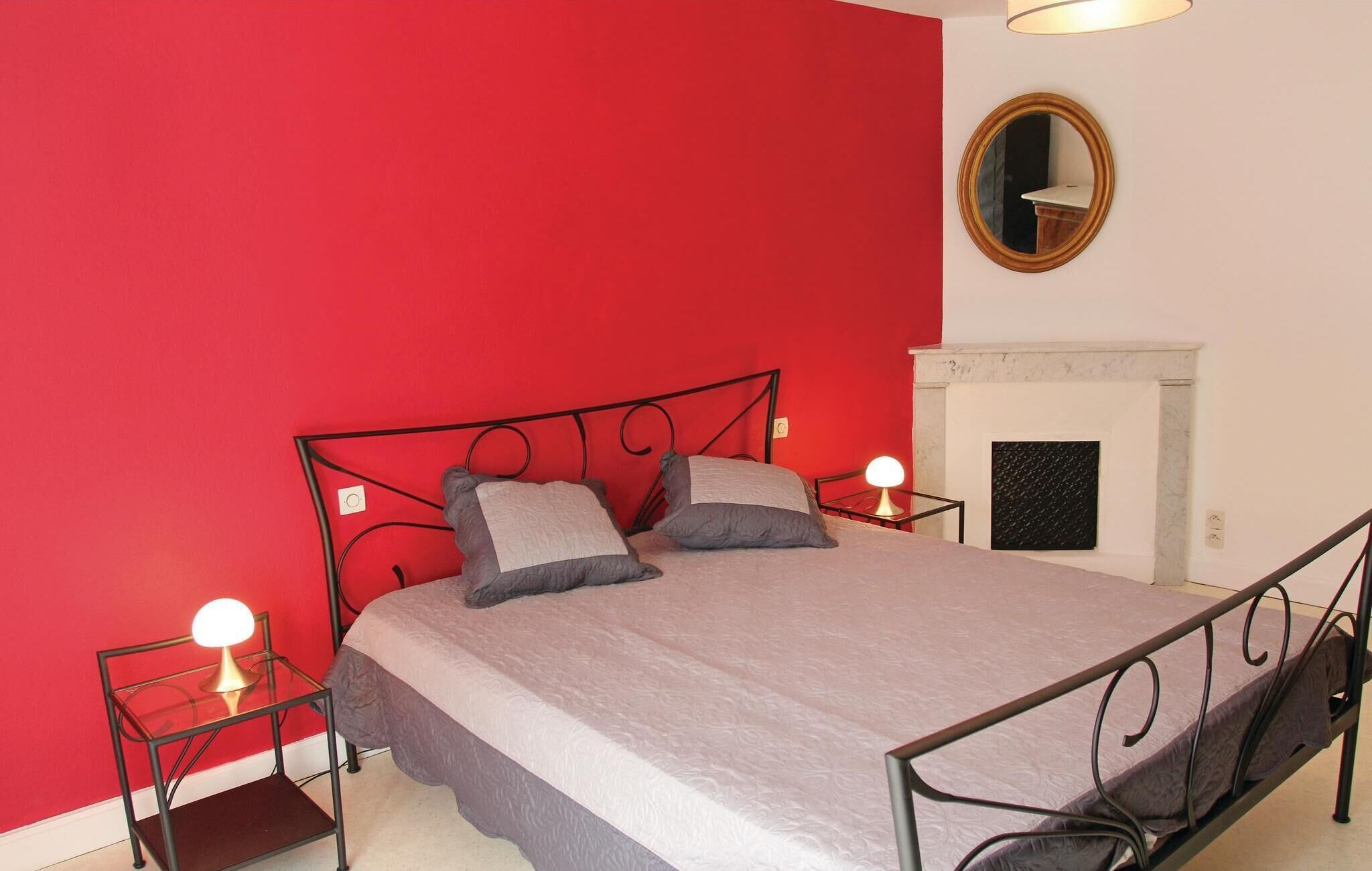 Un lit avec un cadre en métal, deux tables de chevet avec des lampes, une cheminée et un miroir au mur.