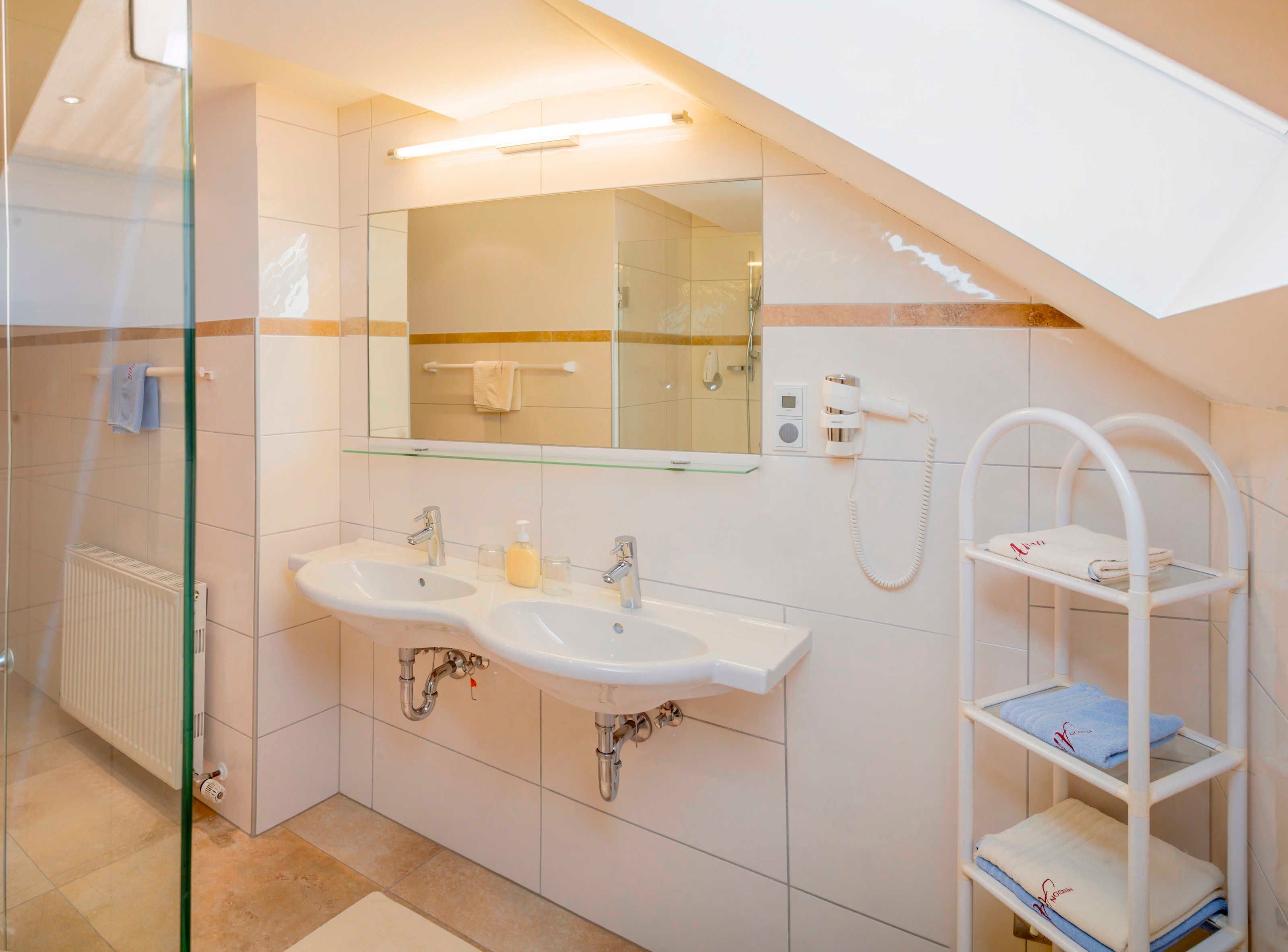 Ein modernes Badezimmer mit zwei Waschbecken, einer Duschkabine aus Glas, einem Handtuchhalter und einer eingebauten Ablage.