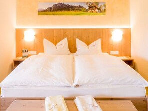 Ein Doppelbett mit weißen Leinentüchern, zwei Nachttische mit Lampen und ein gerahmtes Bild über dem Bett.