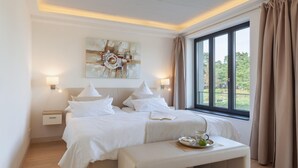 Ein Hotelzimmer mit einem großen Bett, Nachttischen, einer Bank mit Tablett und einem mit Vorhängen versehenen Fenster.