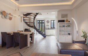 A modern interior with a dining area, a sofa, a staircase, and a kitchen.
