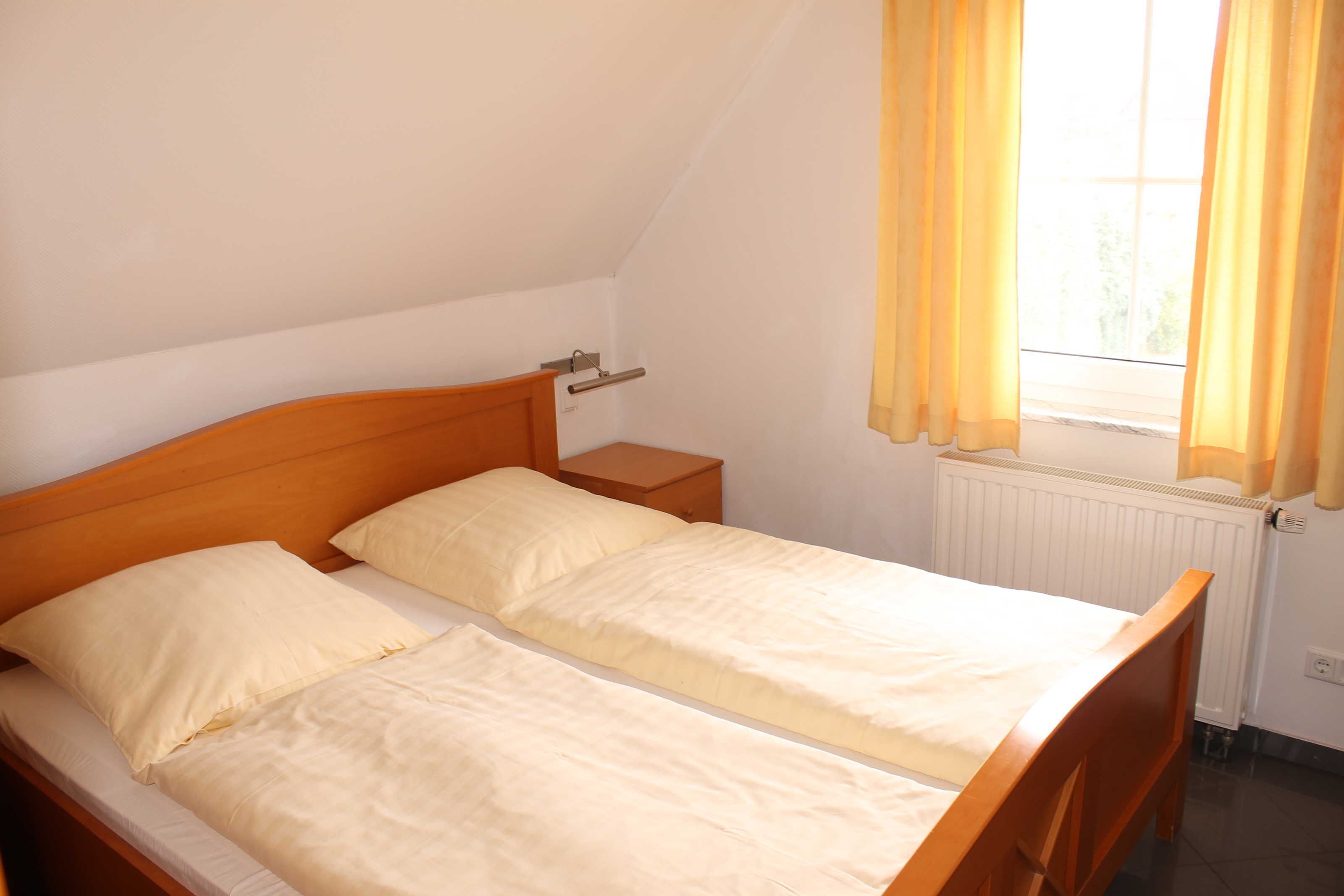Een kleine, schone kamer met een enkel bed, een nachtkastje, een raam met gordijnen en een radiator.