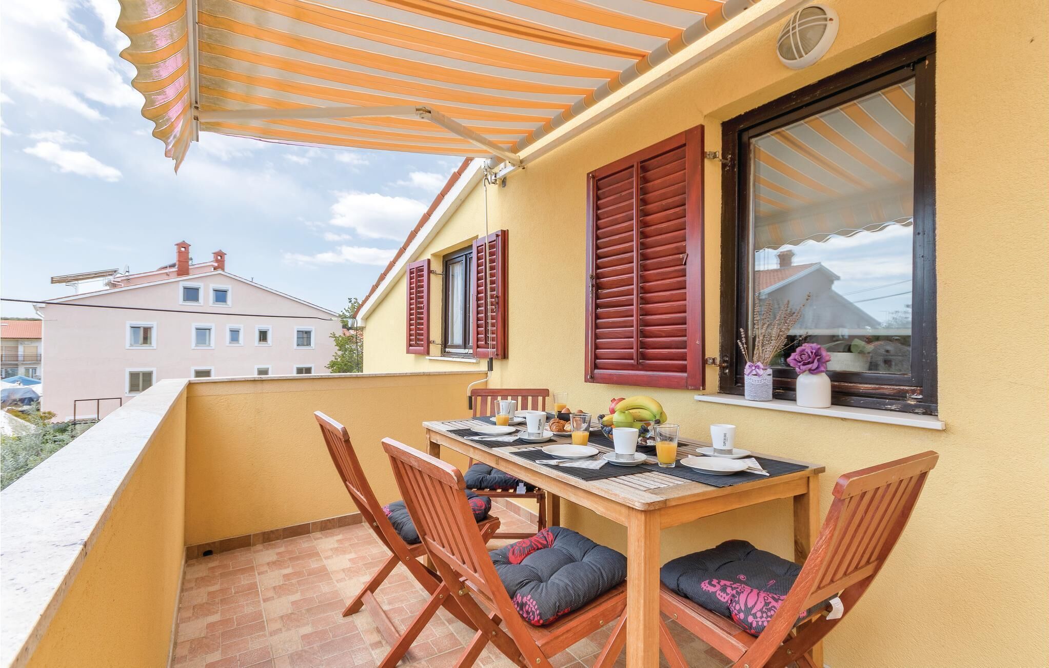 Un balcon avec une table préparée pour le petit-déjeuner, des chaises en bois et un mur jaune.