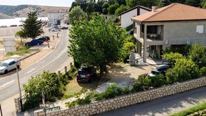 A residential area with a two-story house, a paved road, parked cars, and a stone wall. - Holiday apartment 80 m from the beach (Lopar)
