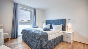 A bedroom with a large bed, a bedside table, a nightstand, a window with curtains, and a view of the outside. - Villa Margarete Whg. 8 - Villa Margarete, BEACH NEXT (Heringsdorf)