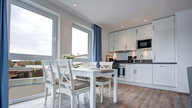 A modern kitchen with white cabinets, a microwave, and a dining area with a table and chairs. - Villa Margarete Whg. 8 - Villa Margarete, BEACH NEXT (Heringsdorf)