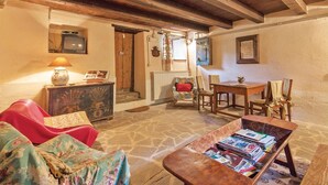 A cozy living room with a stone floor, wooden beams, a red sofa, a wooden coffee table with magazines, a small table with a lamp, and a television on the wall. - Amazing home in Apecchio PU (Apecchio PU)