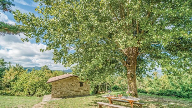 A stone cottage with a picnic table and benches in a grassy area with trees and mountains in the background. - Amazing home in Apecchio PU (Apecchio PU)