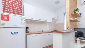 Eine kleine Küche mit weißen Schränken, einem Kühlschrank, einer Kaffeemaschine und einer Holzarbeitsplatte.