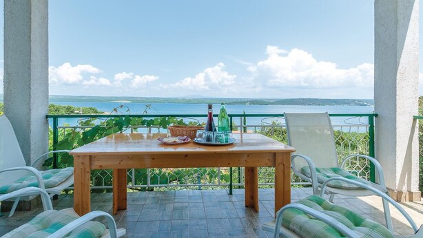 Ein Holztisch mit Blick auf das Meer, umgeben von weißen Stühlen mit grünen Kissen.