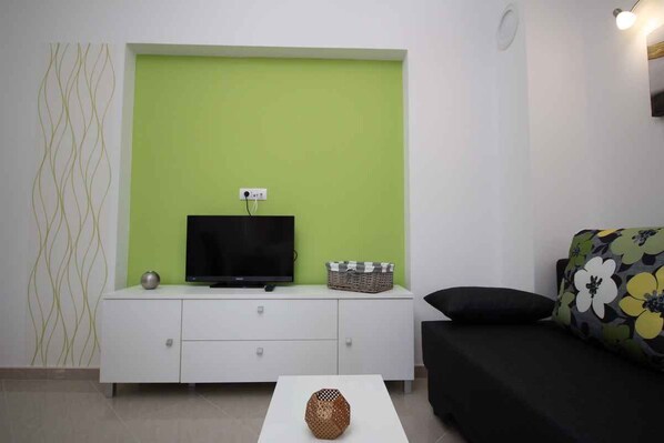 A living room with a green accent wall, a white TV stand, a black sofa, and a white coffee table.