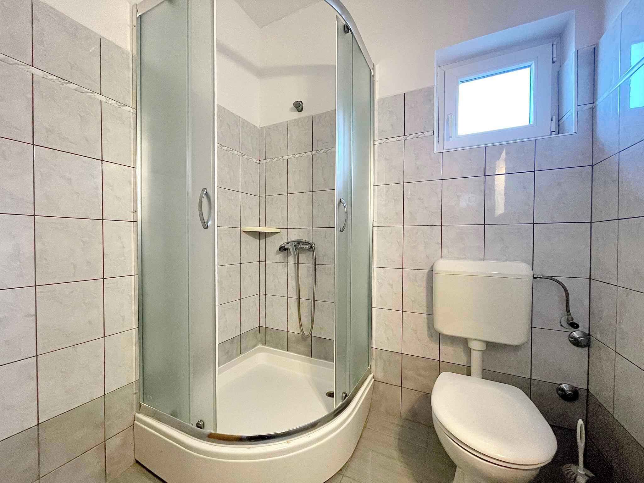 Un baño moderno con cabina de ducha de vidrio, inodoro y ventana sobre el inodoro.