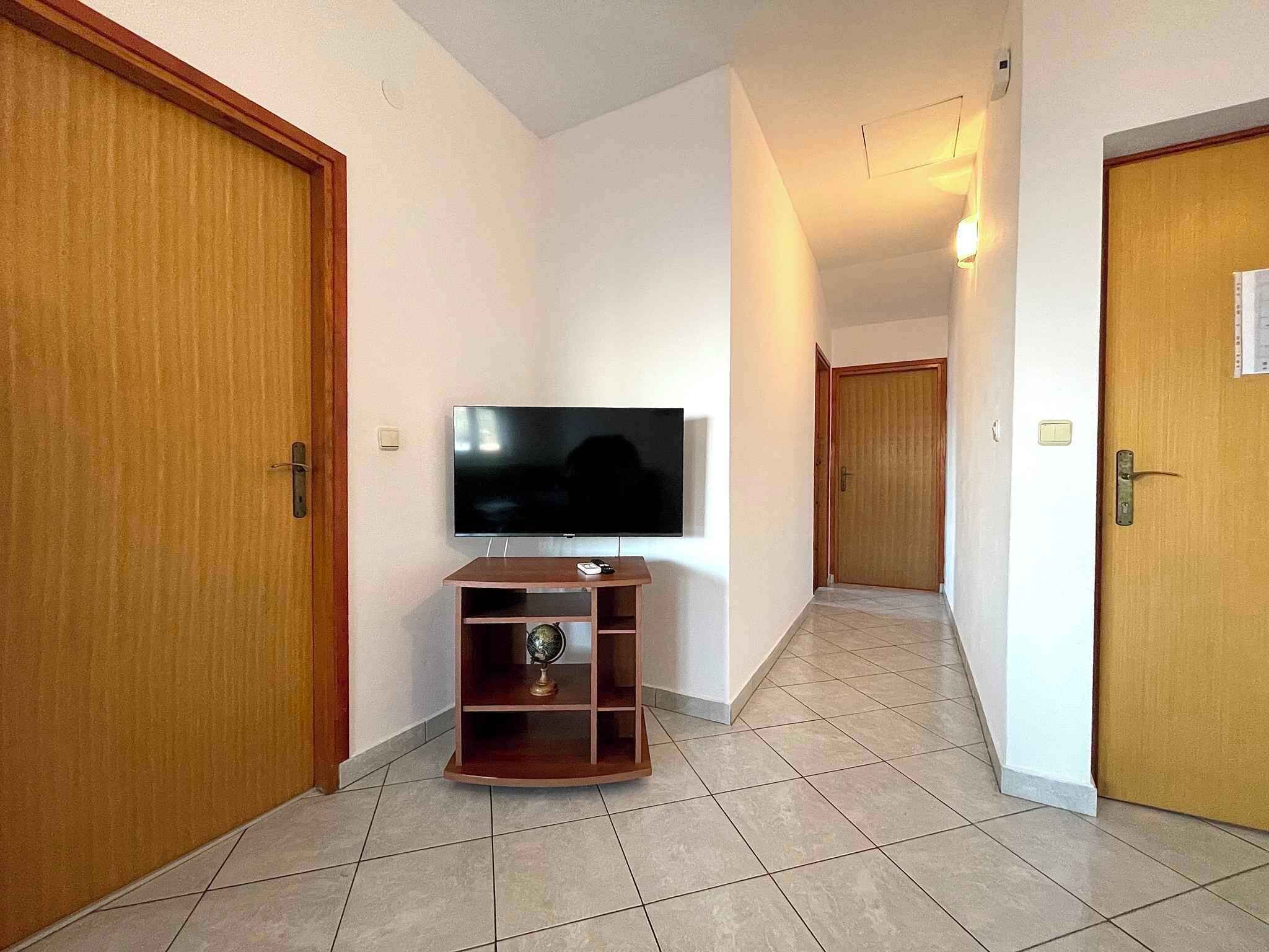 A hallway with a television on a wooden stand, wooden doors, and tiled flooring.