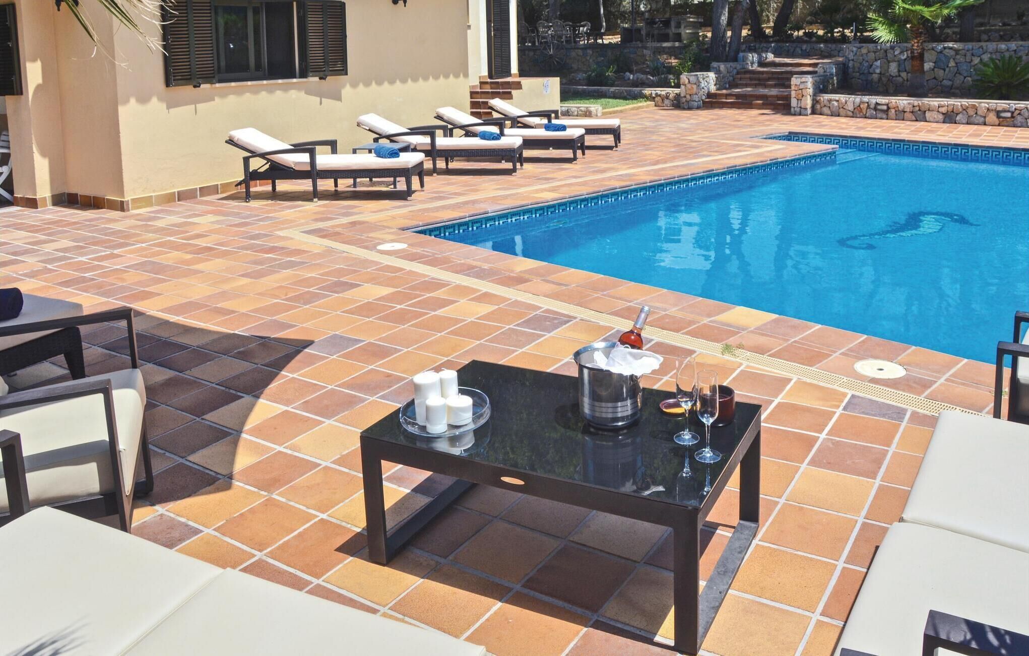A poolside area with lounge chairs, a table with drinks, and a stone wall.