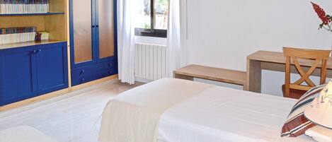 A bedroom with two beds, a wooden desk, a chair, a bookshelf, and a window with curtains.