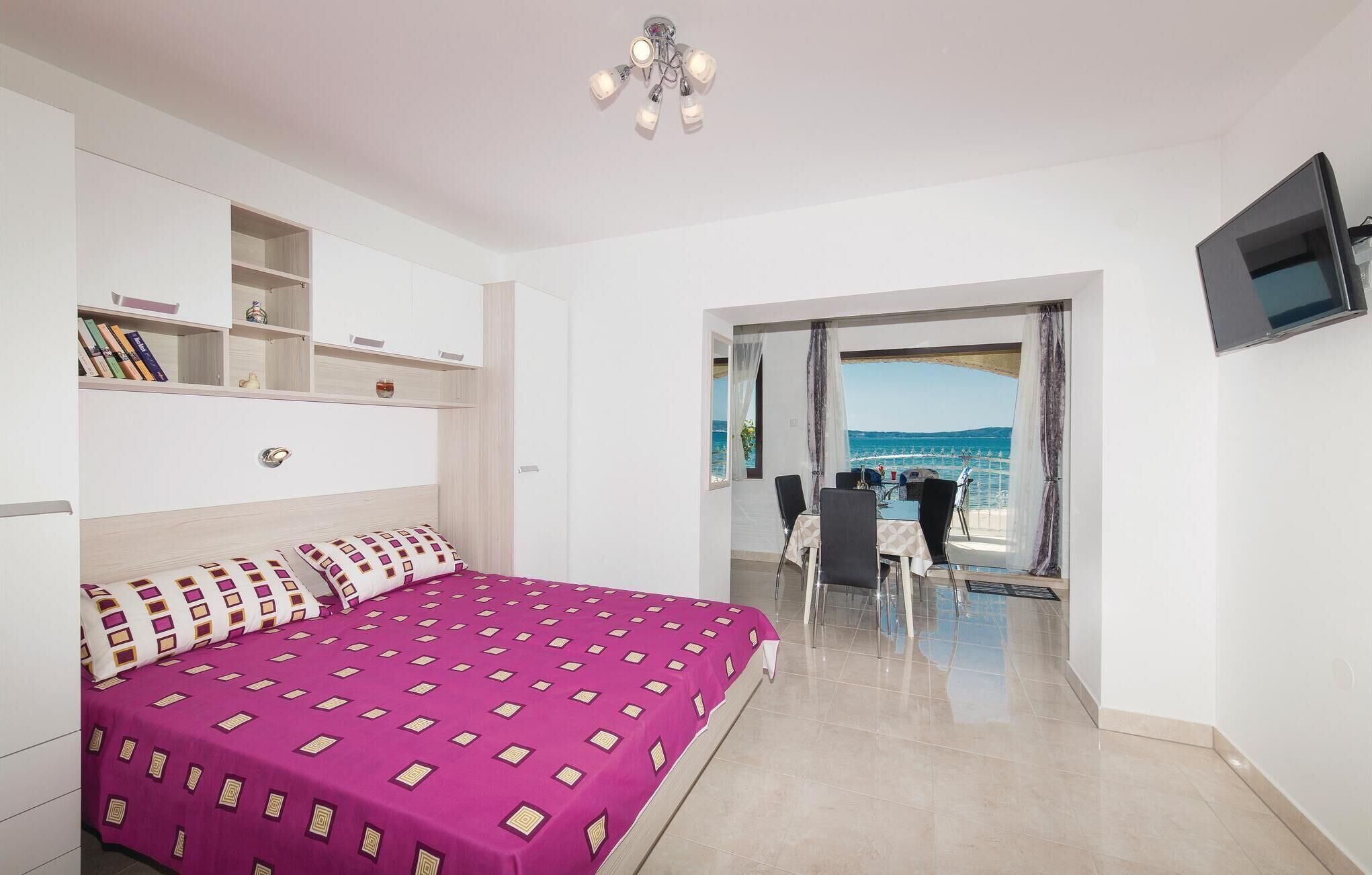 A bedroom with a bed, a TV, a bookshelf, and a view of the sea.