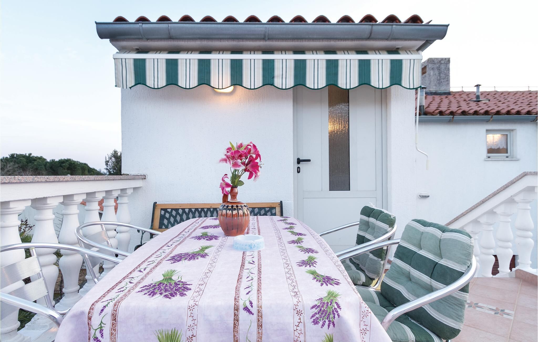 A patio with a table set for two, a chair, a vase with flowers, and a white door.