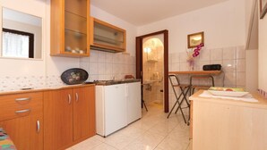 A compact kitchen with wooden cabinets, a white refrigerator, a sink, and a dining area with a chair and table.