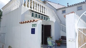 A white building with a balcony, a door, and a small table with a chair and a potted plant.