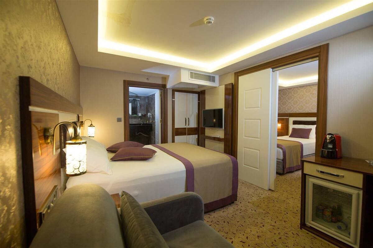 A hotel room with a bed, a desk, a chair, a TV, and a minibar.