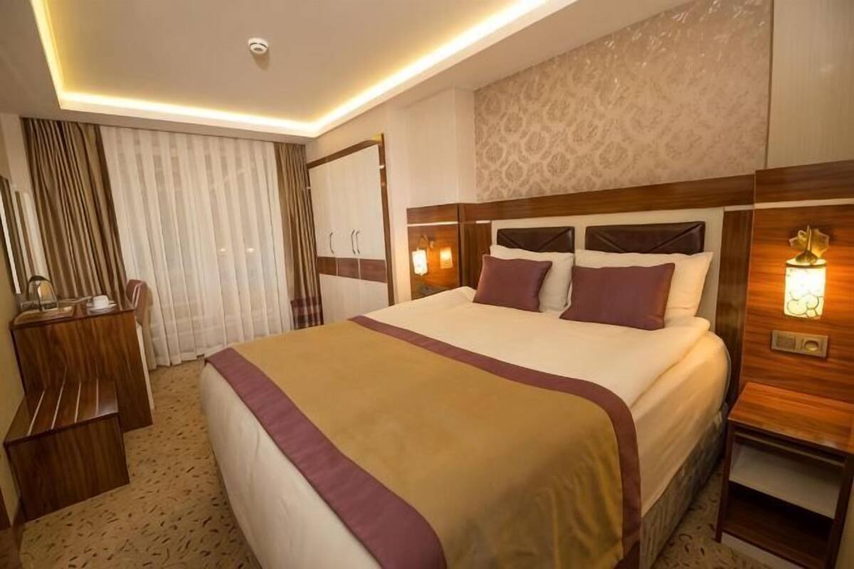 A hotel room with a large bed, a desk, and a wardrobe.
