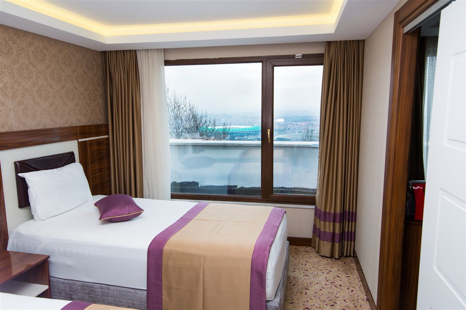 A hotel room with a large bed, a view of the city, and a window with curtains.