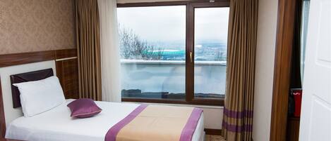 A hotel room with a large bed, a view of the city, and a window with curtains.