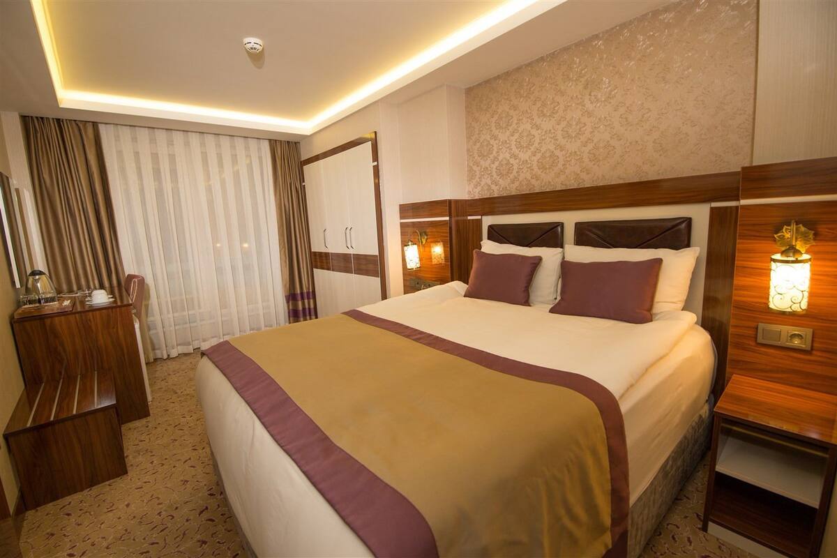 A hotel room with a large bed, bedside tables, a desk, and a wardrobe.