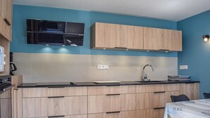 Een moderne keuken met een blauwe wand, houten kastjes, een zwart aanrecht en een ingebouwde magnetron.