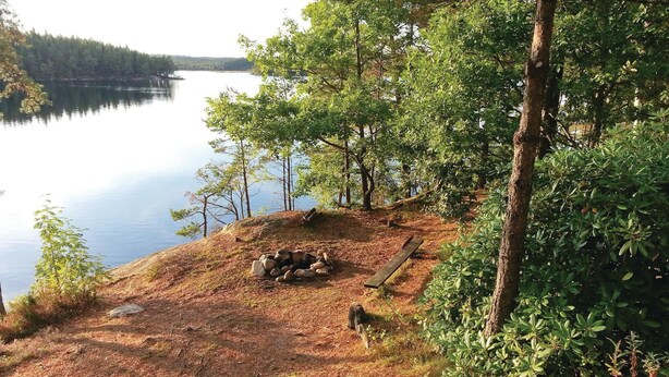 En campingplats vid sjön med en eldstad och fri utsikt över vattnet.