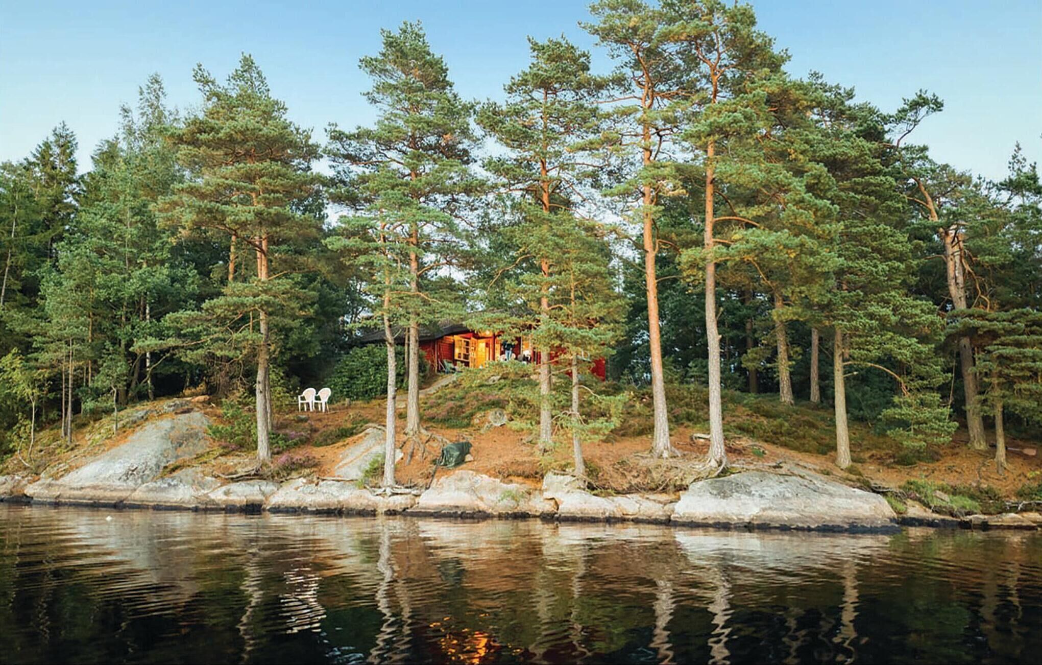 Une cabane entourée de grands pins, avec un petit quai qui s’avance sur un lac paisible.
