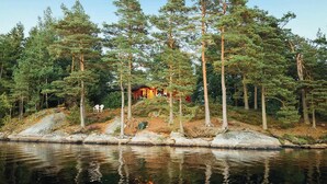 En stuga omgiven av höga tallar, med en liten brygga som sträcker sig ut i en stilla sjö.