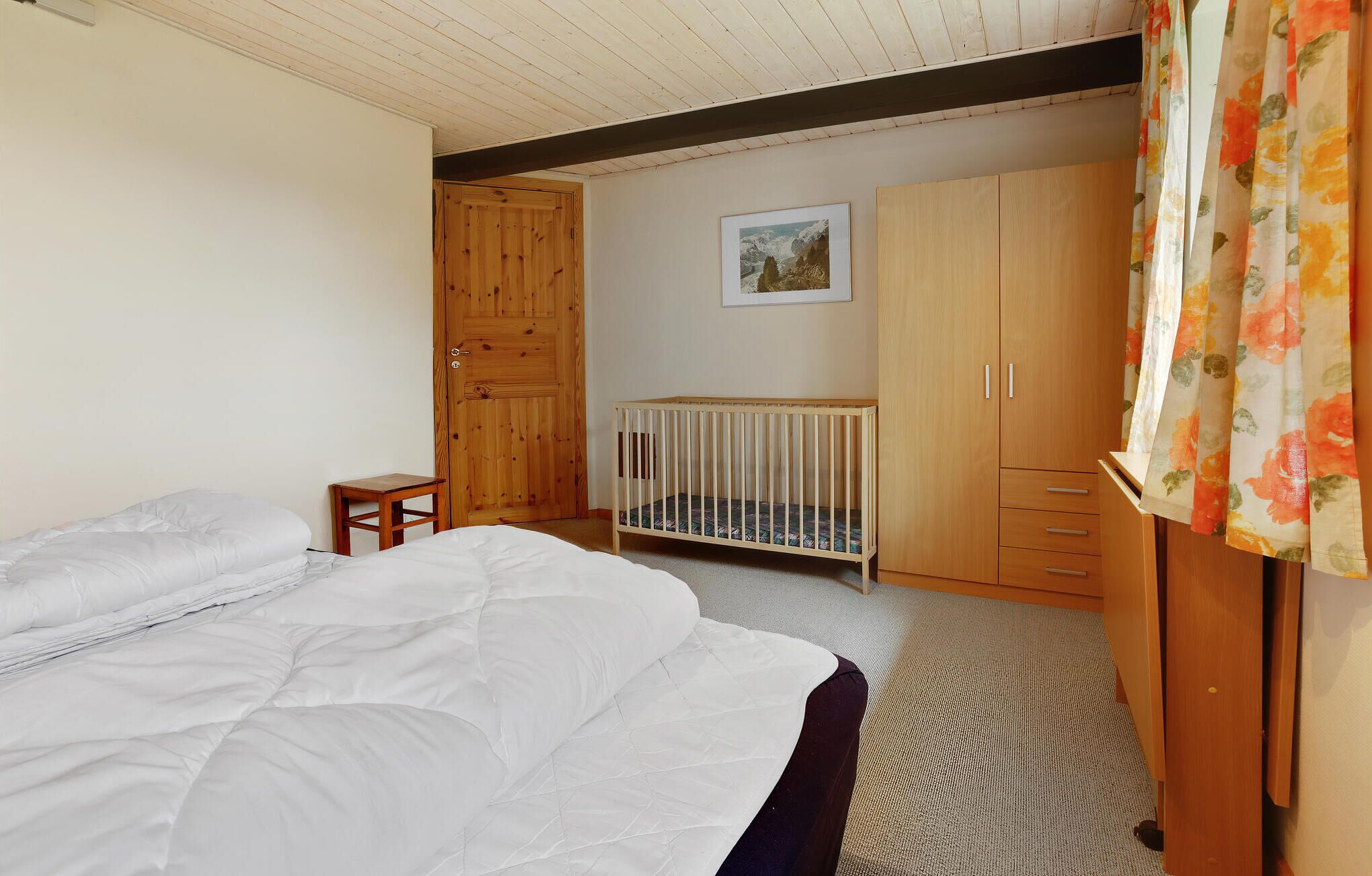 A bedroom with a bed, a crib, wooden wardrobe, and a painting on the wall.