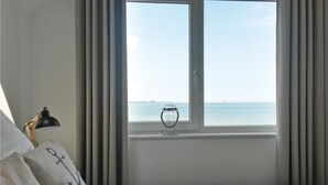 Una camera d'albergo con un letto, una lampada, una finestra vista mare e un vaso sul davanzale.
