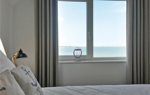 Ein Hotelzimmer mit Bett, Lampe, Fenster mit Meerblick und einer Vase auf der Fensterbank.