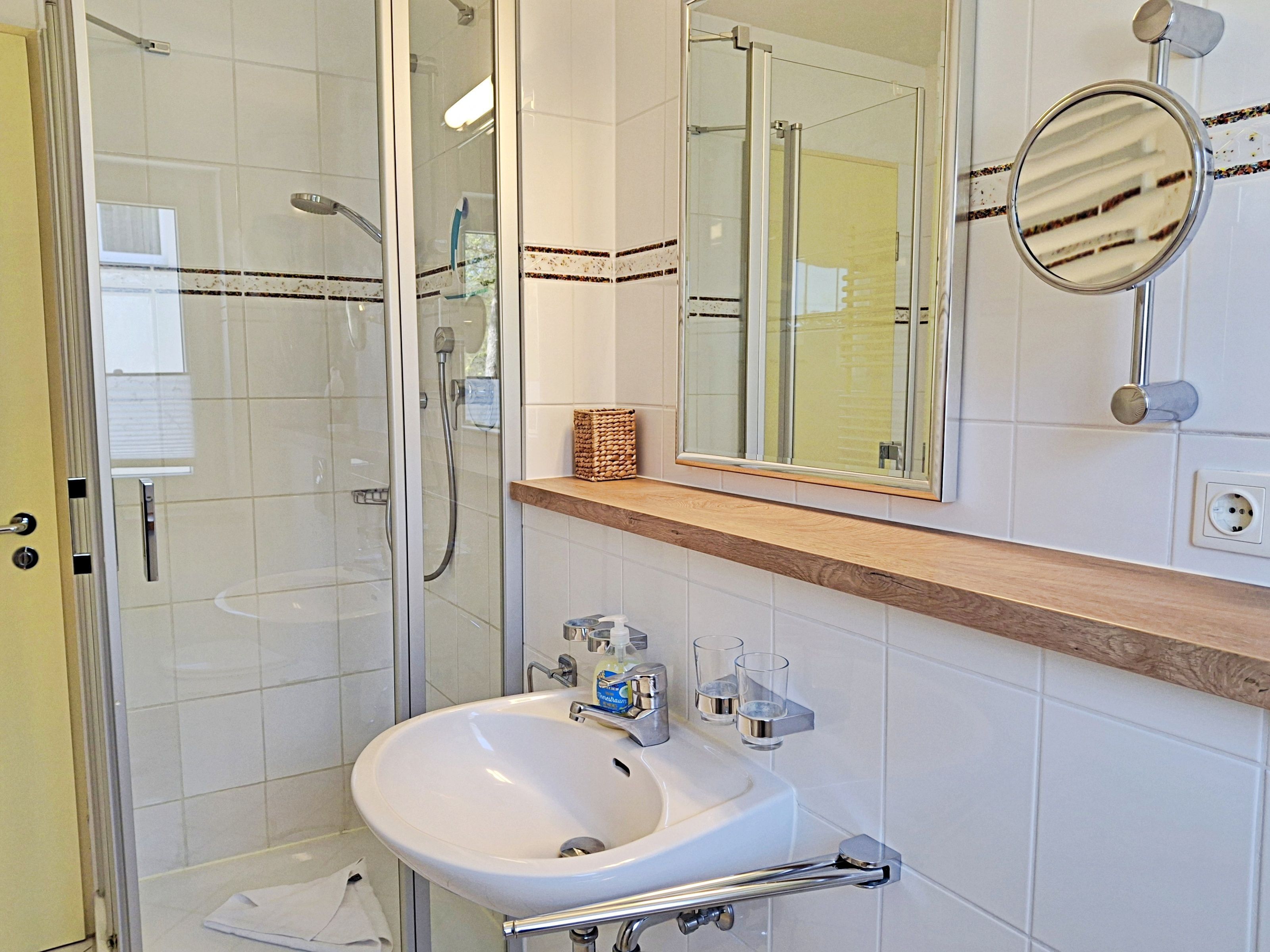 Un baño con ducha de vidrio, un lavabo blanco con dispensador de jabón y un espejo con iluminación.