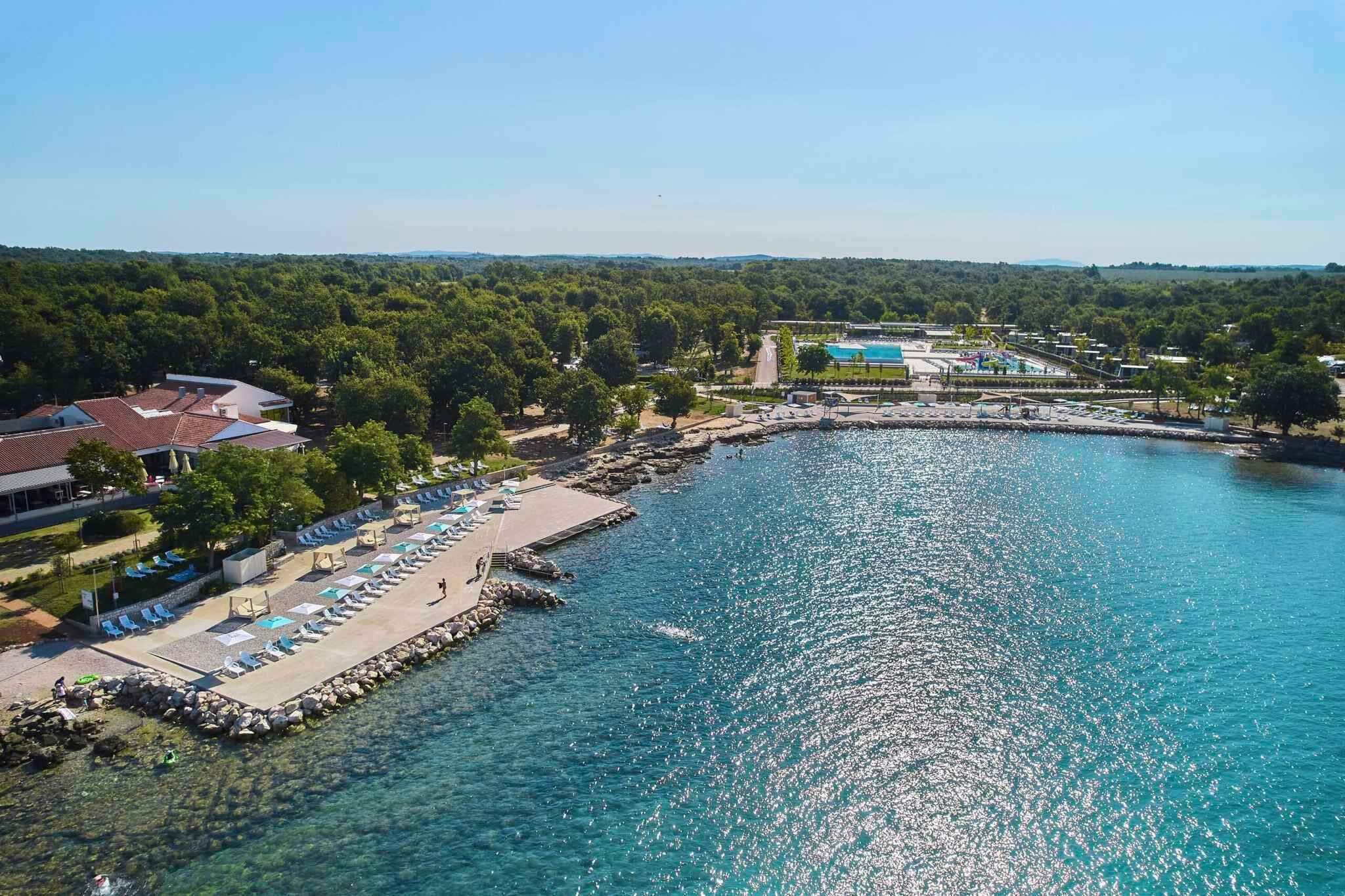 Vista aerea di un resort costiero con piscina, lettini e un litorale roccioso.