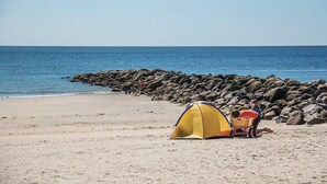 Une plage avec une tente jaune et une chaise rouge près d’une côte rocheuse.