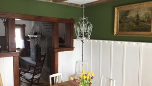 Un coin repas avec une table en bois, des chaises blanches, un lustre et un tableau accroché au mur.