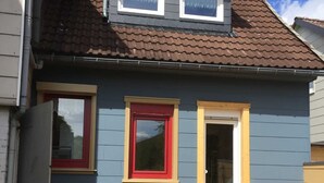 Une maison à deux étages avec une fenêtre à cadre rouge, une fenêtre à cadre blanc et une porte.