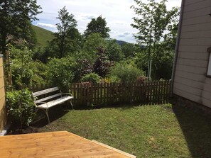 A wooden deck, a bench, a wooden fence, and a grassy yard with trees and shrubs.