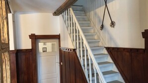 Un escalier en bois avec des rampes blanches menant à une porte ornée d’un miroir et d’un tableau encadré.