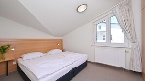 Un dormitorio con cama, mesita de noche, ventana con cortinas y radiador.